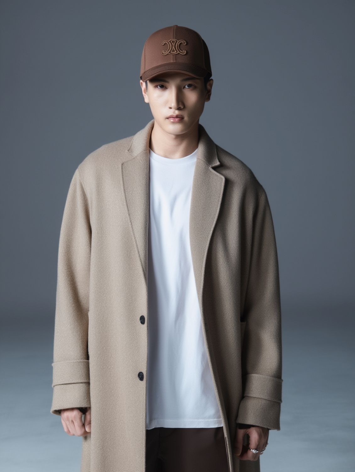 Person wearing a beige coat and Celine Triomphe Baseball Cap in Cotton Gabardine Tiramisu 2AUG4234X.GAA7 against a gray background