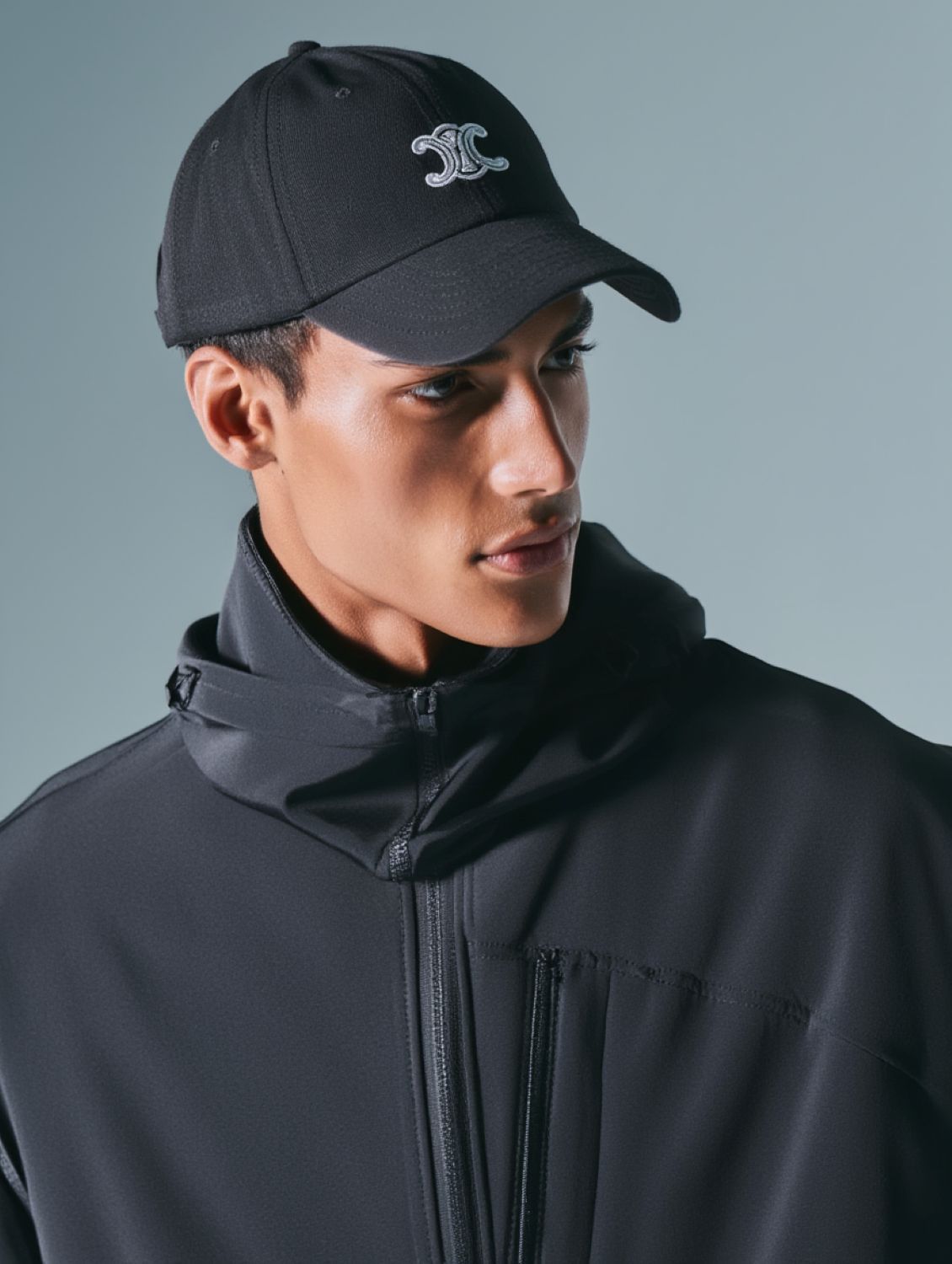 Person wearing a Celine Vivienne Cap in Cotton Twill Black & White AA0GV2U74.37BW with a triomphe logo and black jacket against a gray background