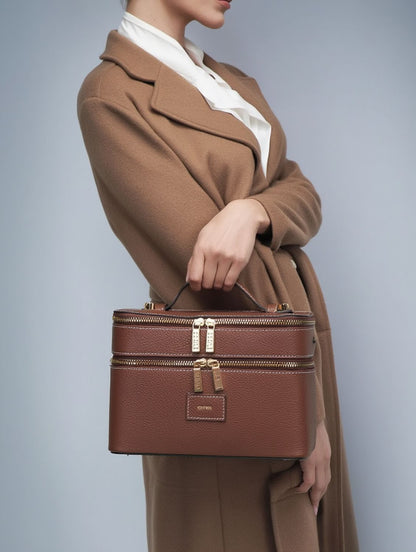 Person wearing a brown coat holding a Etoile Duo Vanity Case Ginger Brown against a gray background