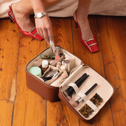 Open Etoile Duo Vanity Case Ginger Brown on wooden floor with person's hand reaching in