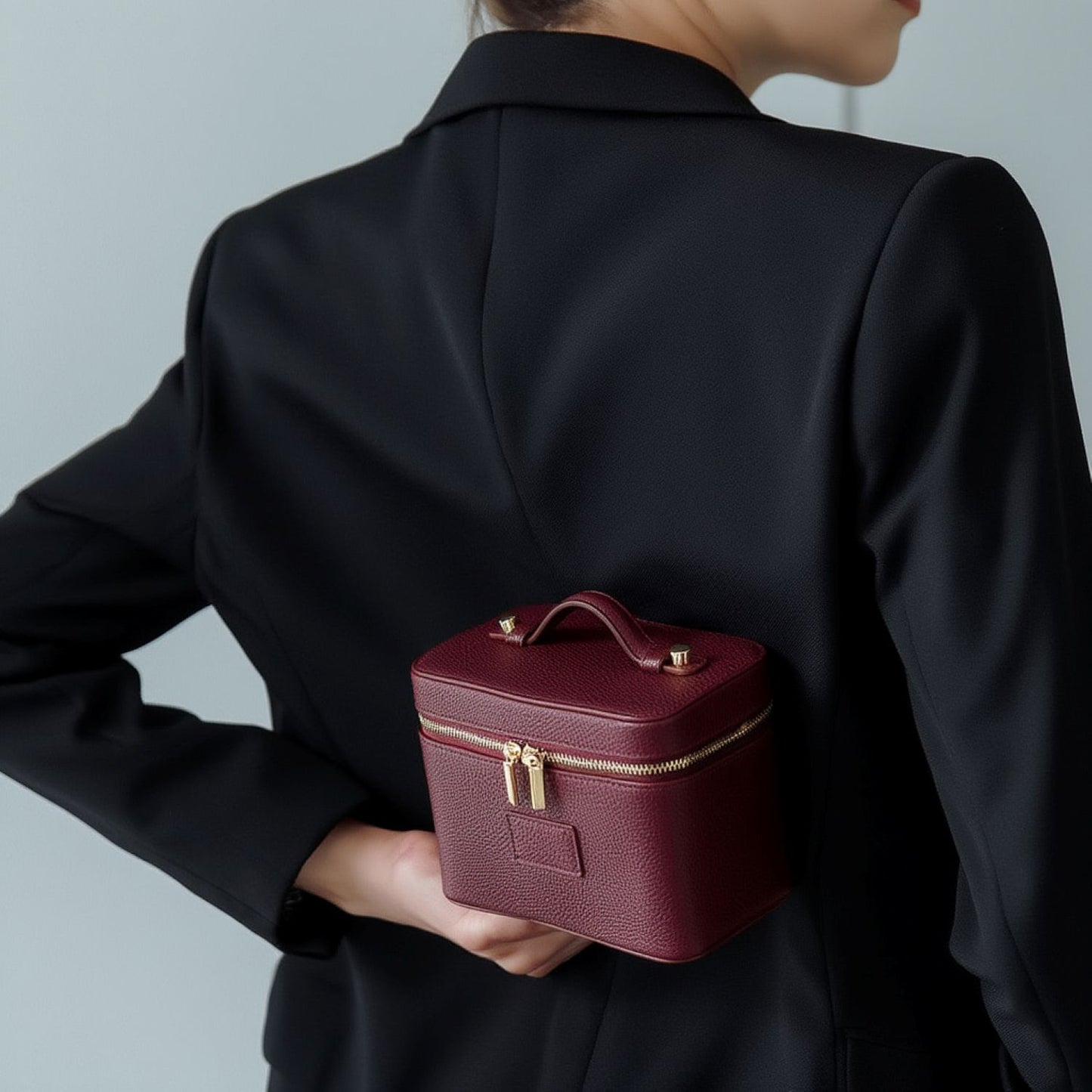 Person holding a Etoile Mini Vanity Case Burgundy with gold accents against a neutral background