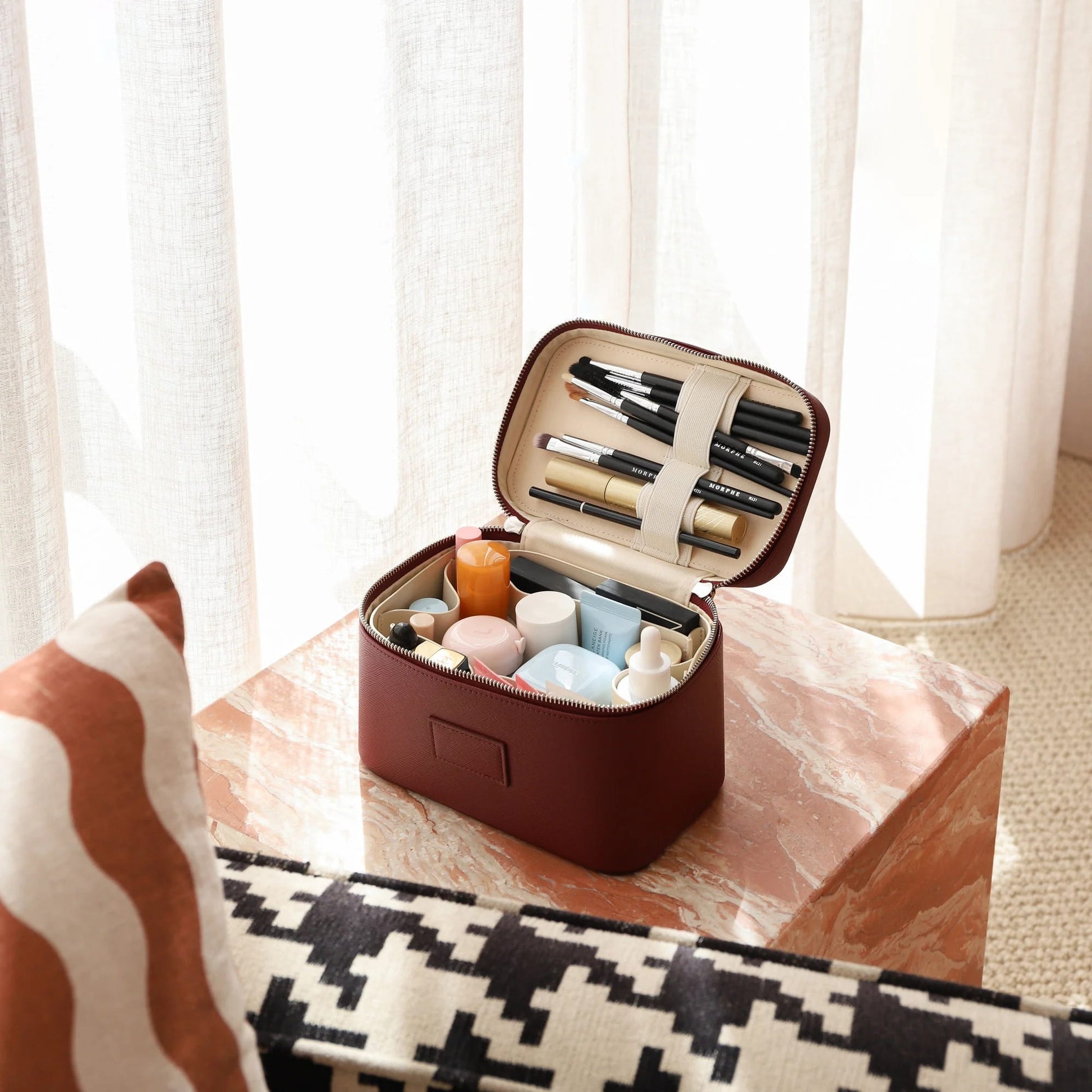 Open Etoile Mini Vanity Case Burgundy with makeup items on a marble surface with curtains in the background