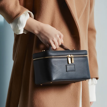 Person holding a Etoile Vanity Case Black with gold zipper against a neutral background