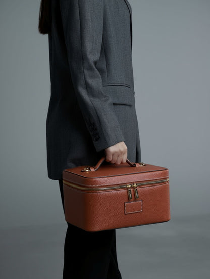 Person holding a Etoile Vanity Case Ginger Brown against a gray background
