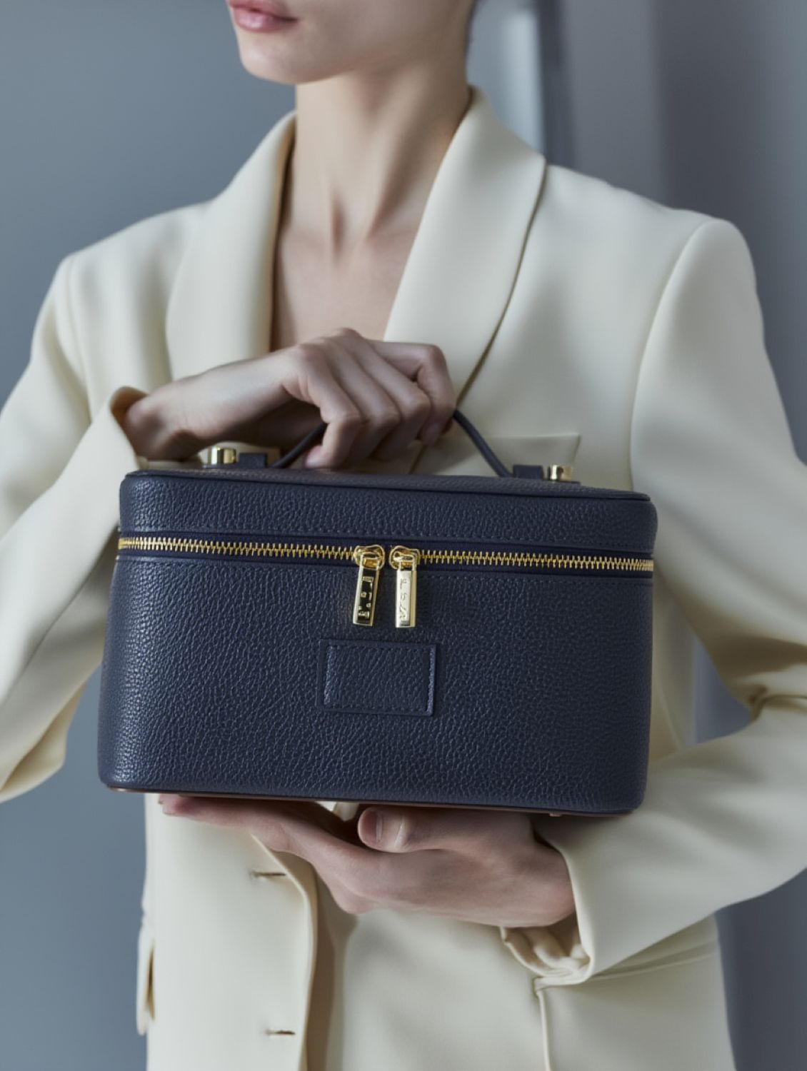 Person holding a Etoile Vanity Case Navy with gold zippers against a neutral background