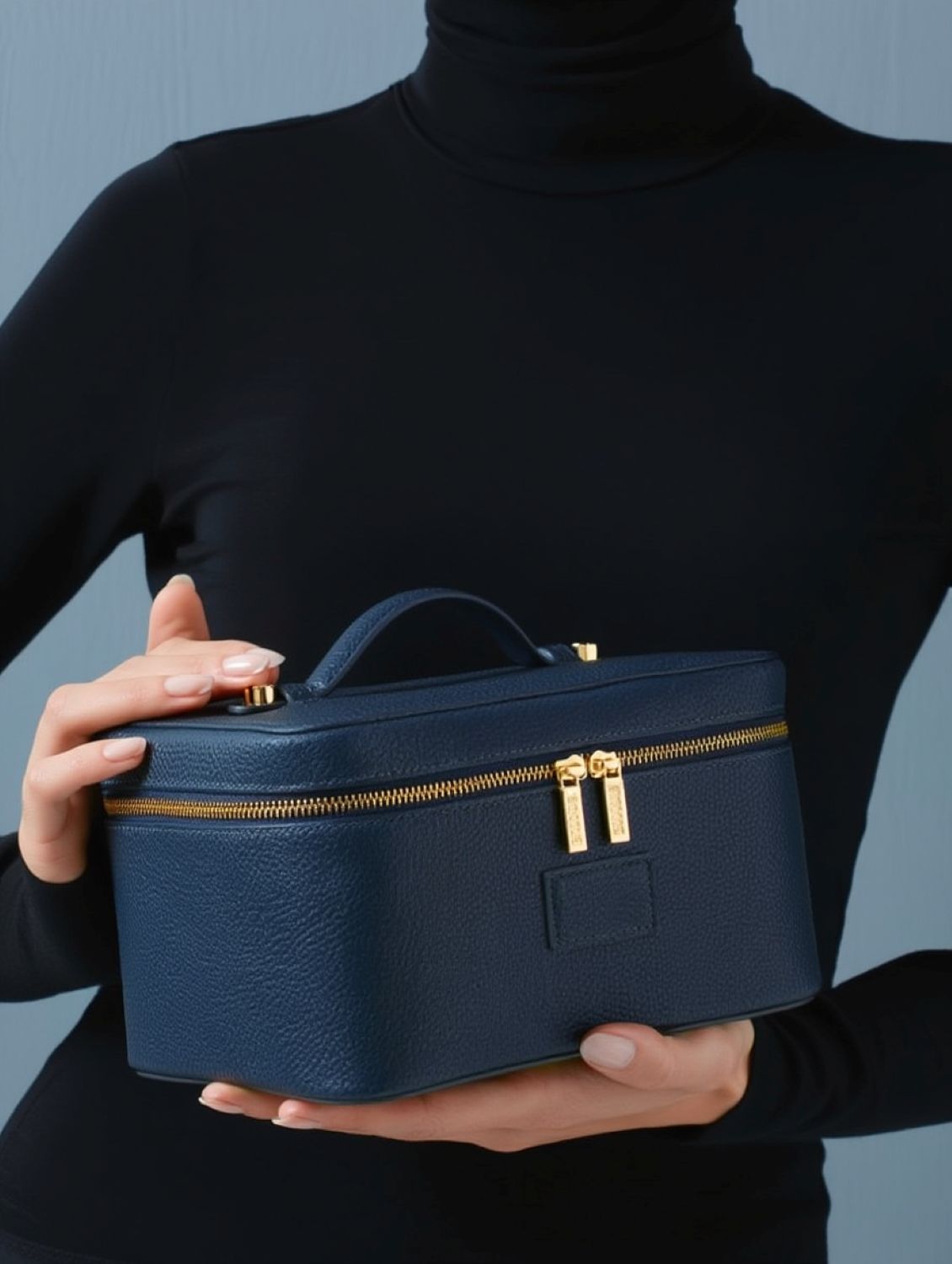 Person holding a Etoile Vanity Case Navy with gold zippers against a gray background