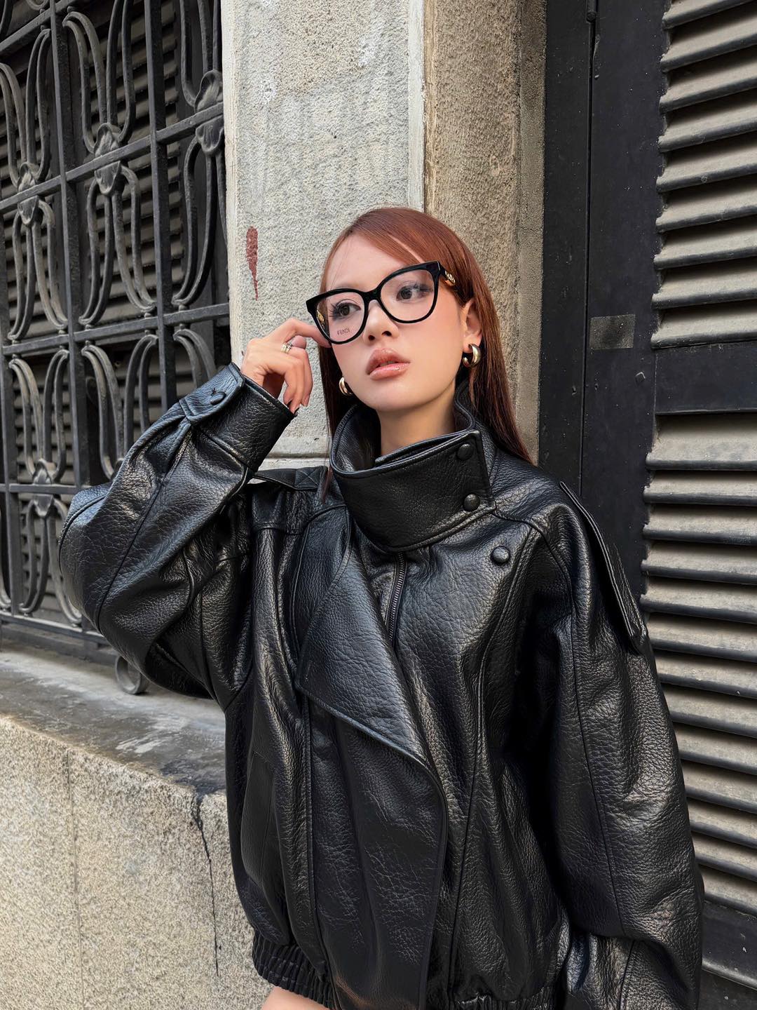 Person wearing a black leather jacket and Fendi FE50093I-001 O'Lock Round Black Eyeglasses standing against a textured wall.