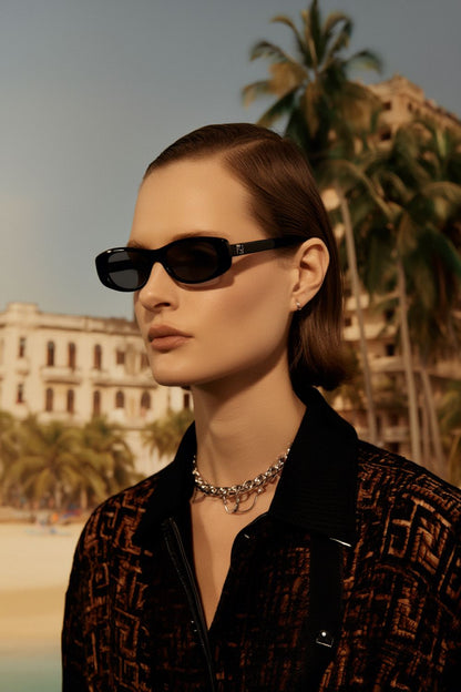Woman wearing Fendi FE40183I 01A — FF Black Oval Sunglasses with palm trees and buildings in the background