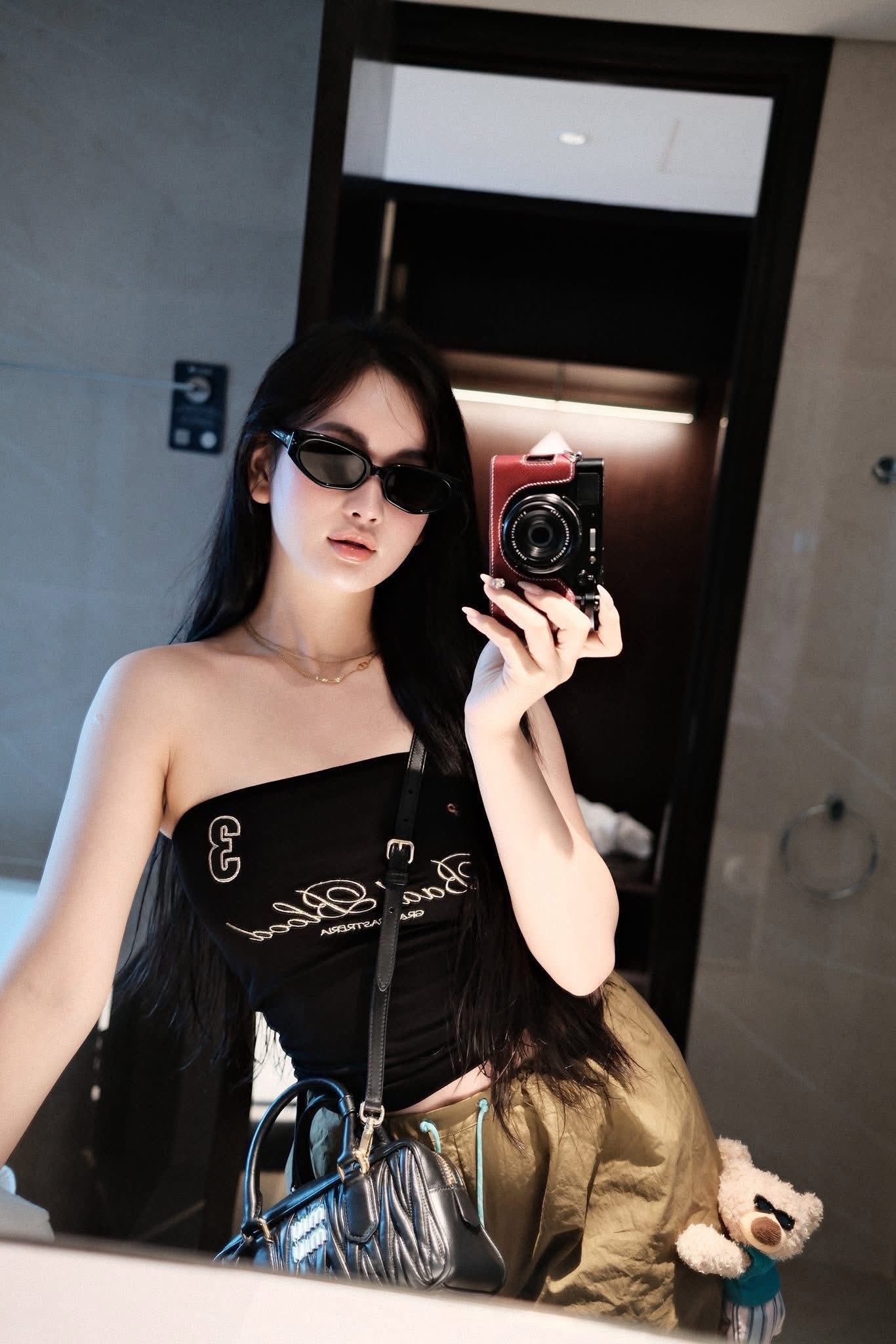 Woman holding a camera in front of a mirror, wearing Gentle Monster (GM) Duns 01 and a black outfit.