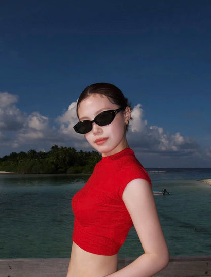 Woman in a red top and Gentle Monster (GM) Miro 01 standing on a beach with ocean and sky in the background