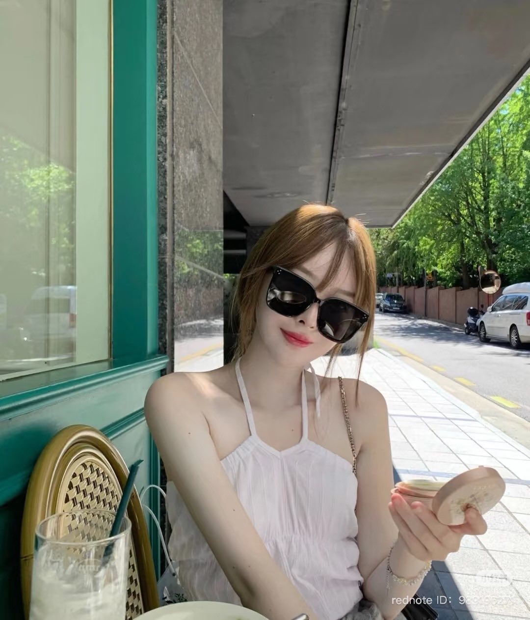 Woman wearing Gentle Monster (GM) New Her T1 and a white top sitting outdoors near a building.