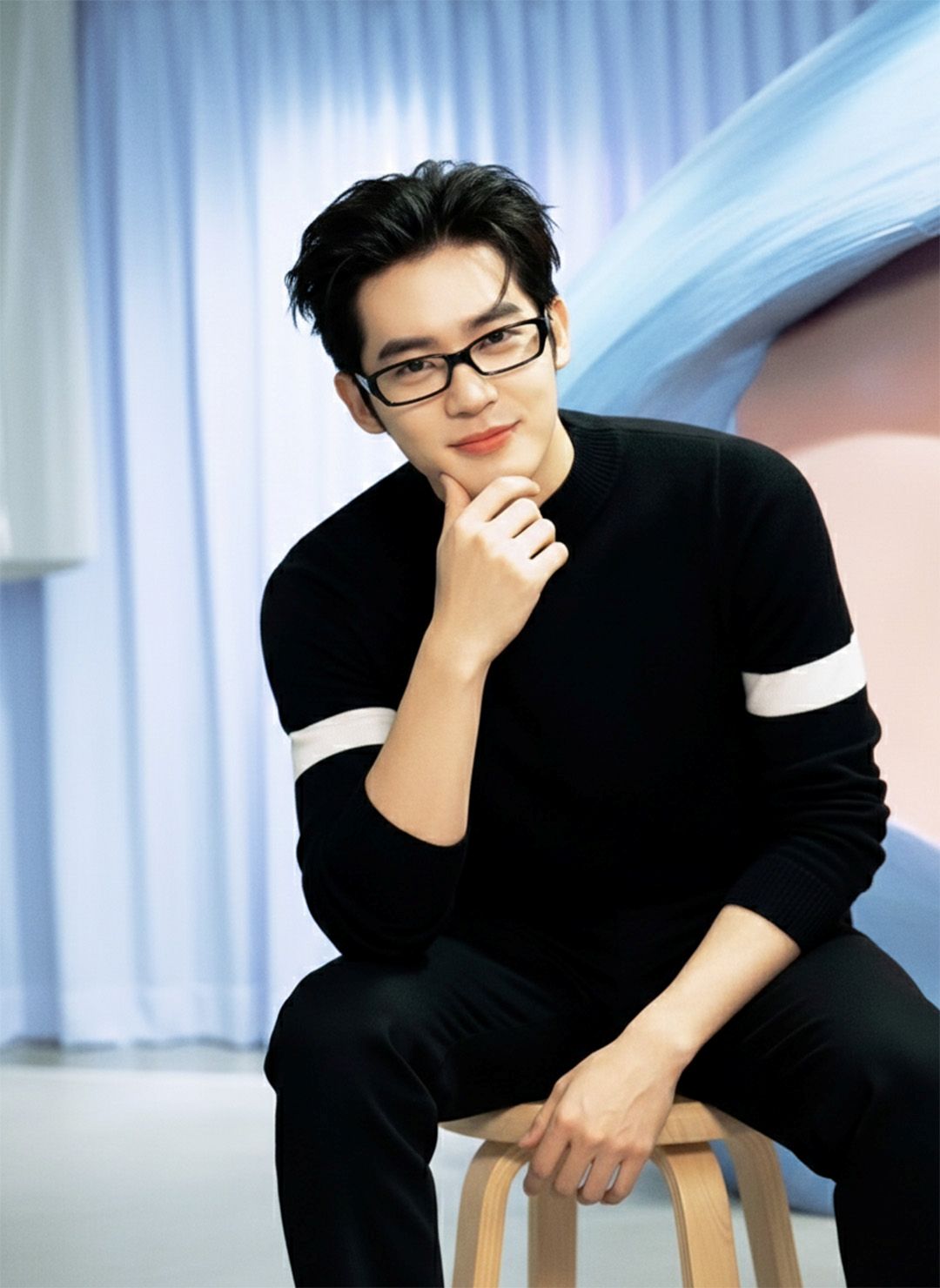 Man wearing Gentle Monster Halo G18 and a black sweater sitting on a stool with a blurred background