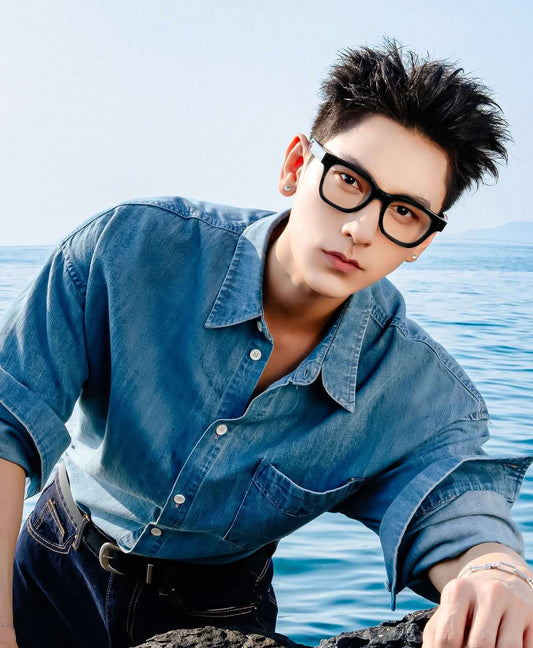 Isaac wearing a denim shirt and Gentle Monster Karl 01 Square Optical Glasses with a blue background