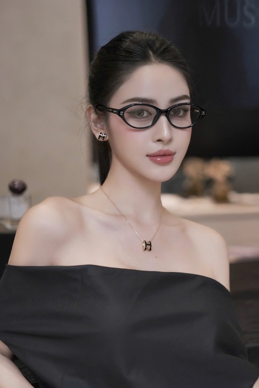 Woman wearing Gentle Monster La Cha 01(C) Round Optical Glasses and a black off-shoulder top in an indoor setting