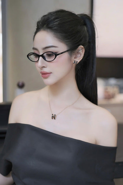 Woman wearing Gentle Monster La Cha 01(C) Round Optical Glasses and a black off-shoulder top with a blurred indoor background