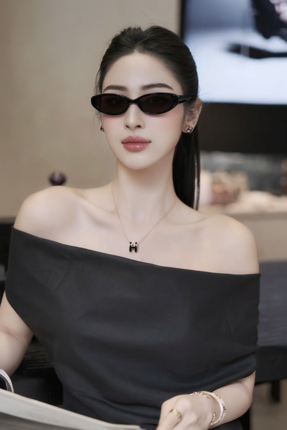 Woman wearing a black off-shoulder top and Gentle Monster Monica 01 Cat-Eye Sunglasses indoors.