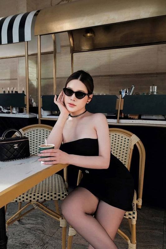 Woman wearing Gentle Monster Mowa 01 Cat-Eye Sunglasses in a black dress sitting at a table in a stylish interior setting.