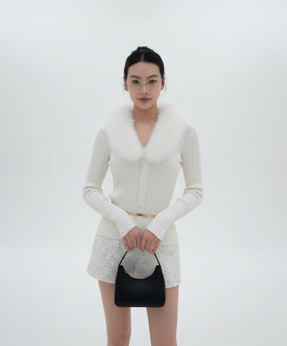 Woman wearing Gentle Monster Origami 031 in a white knit outfit with fur collar and holding a black handbag on a white background