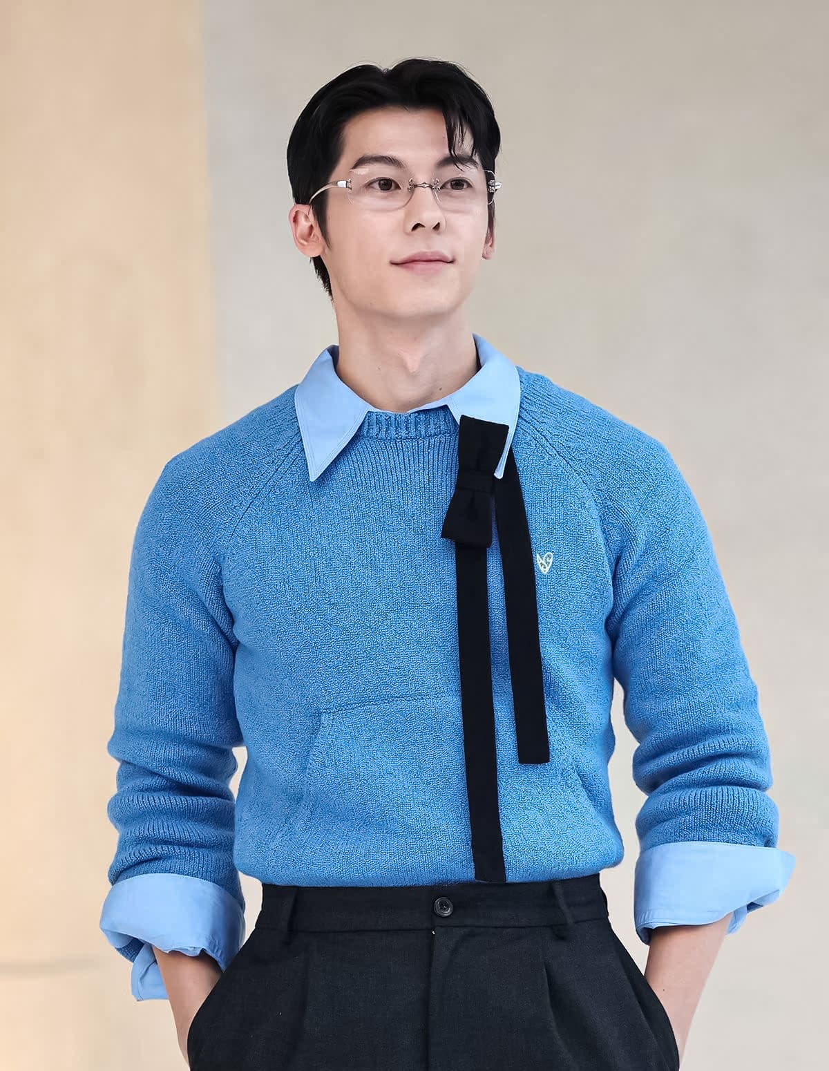 Hứa Quang Hán wearing a Gentle Monster Paranoyd 02(CM) Square Glasses and blue sweater with a black tie over a light blue shirt against a beige background