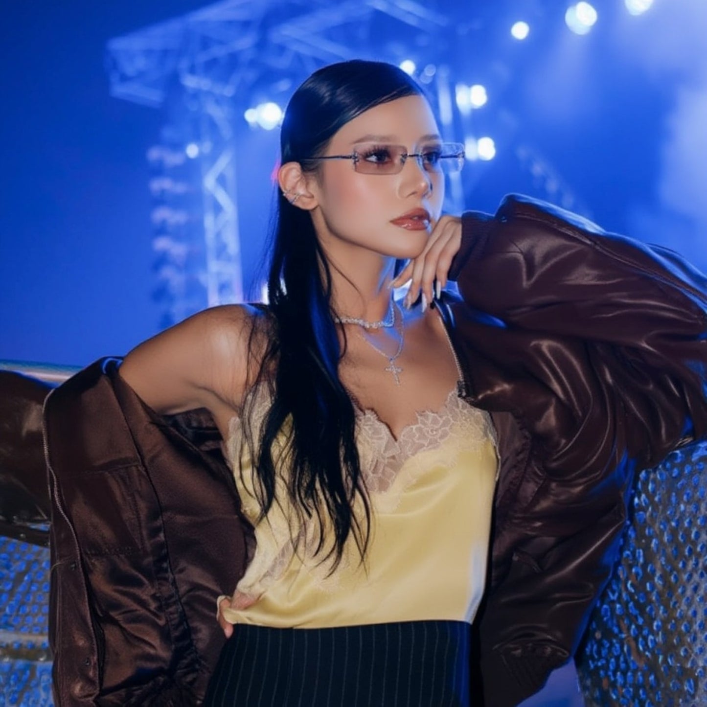 Woman wearing a Gentle Monster Paranoyd 02(GM) Square Glasses, yellow top and brown jacket with a blue background