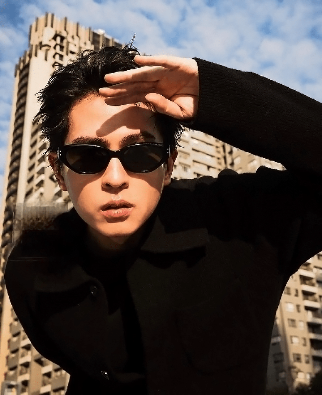 Person wearing Gentle Monster (GM) Rococo 01 and a black coat with a cityscape background