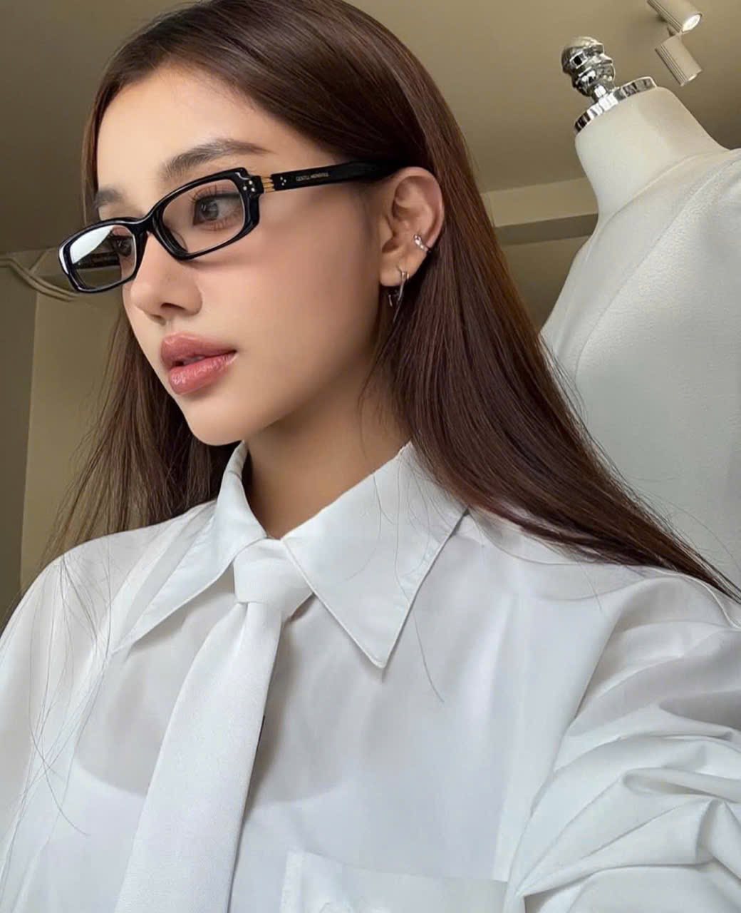 Woman wearing Gentle Monster - GM Slyk 01 (Light Adaptive) and a white shirt with a tie in front of a mannequin