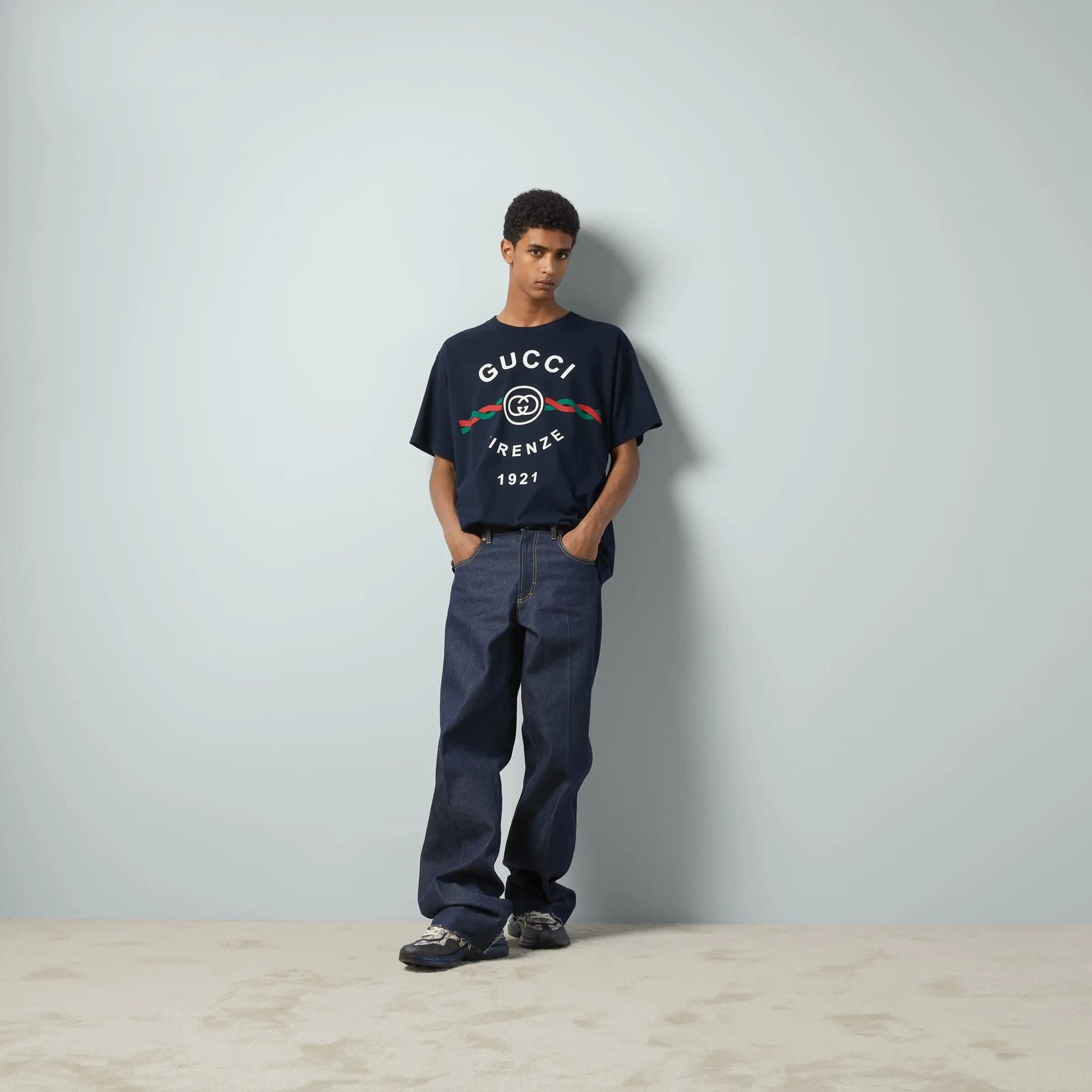 Person wearing a Gucci Cotton Jersey Gucci Firenze 1921 T-shirt in Navy 616036 XJD7T 4795 and pants against a plain background