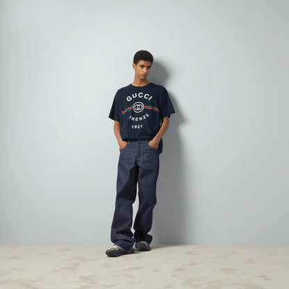 Person wearing a Gucci Cotton Jersey Gucci Firenze 1921 T-shirt in Navy 616036 XJD7T 4795 and pants against a plain background