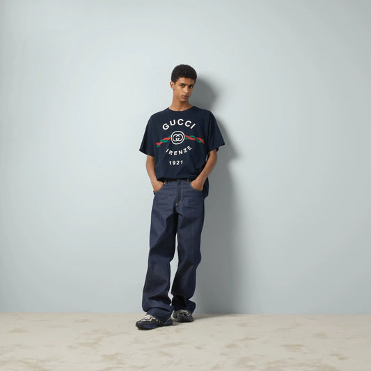Person wearing a Gucci Cotton Jersey Gucci Firenze 1921 T-shirt in Navy 616036 XJD7T 4795 and pants against a plain background