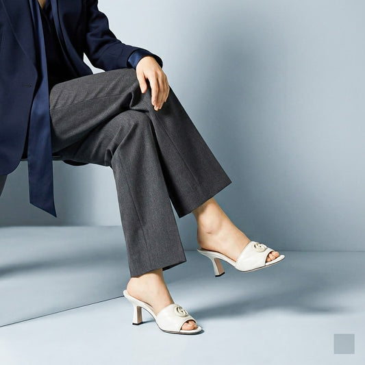 Person wearing a navy blazer and gray pants with Gucci Double G Mid-Heel Slide Sandals White 739133 BKO00 9049 on a light blue background