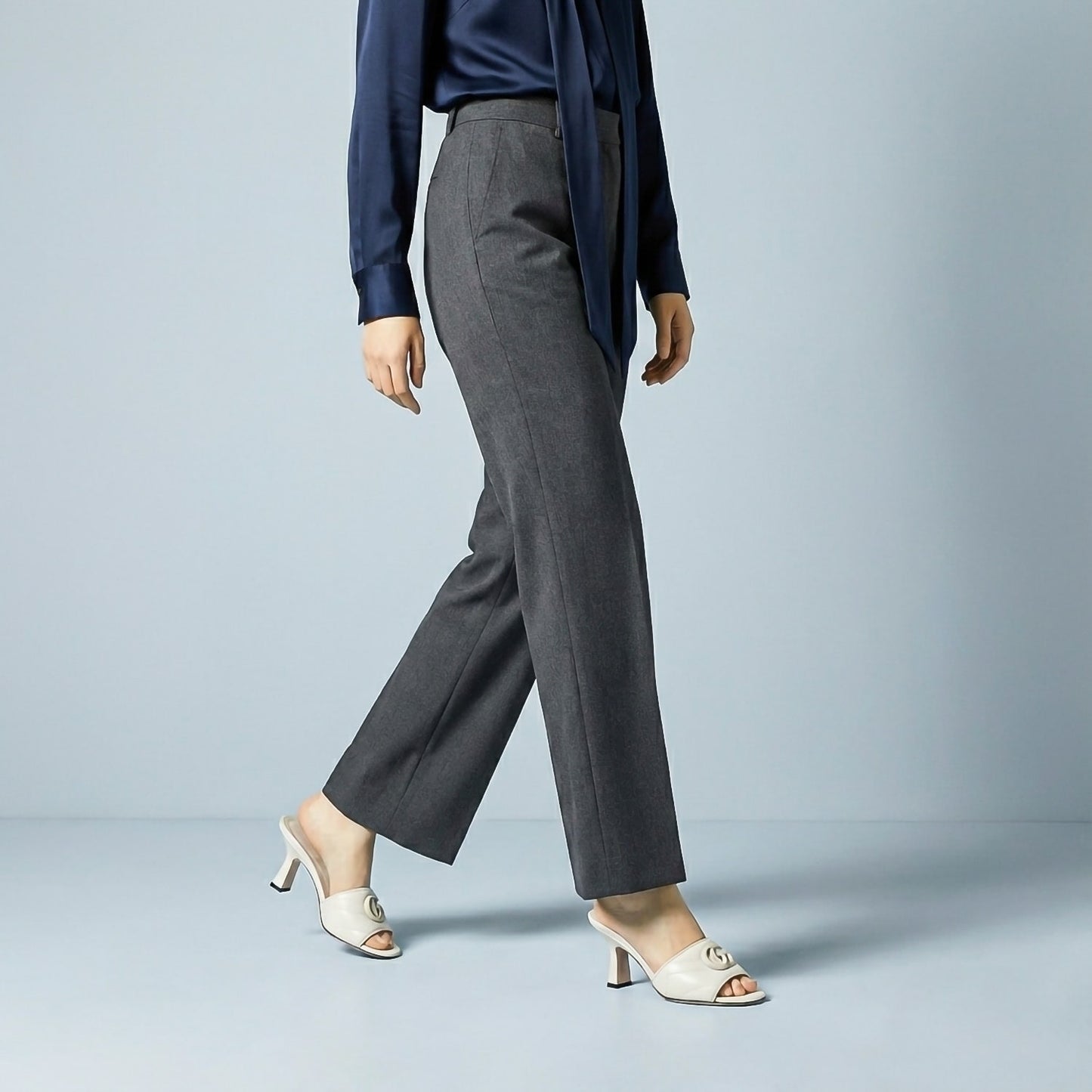 Person wearing a navy blazer and gray pants with Gucci Double G Mid-Heel Slide Sandals White 739133 BKO00 9049 on a light blue background