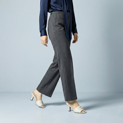 Person wearing a navy blazer and gray pants with Gucci Double G Mid-Heel Slide Sandals White 739133 BKO00 9049 on a light blue background