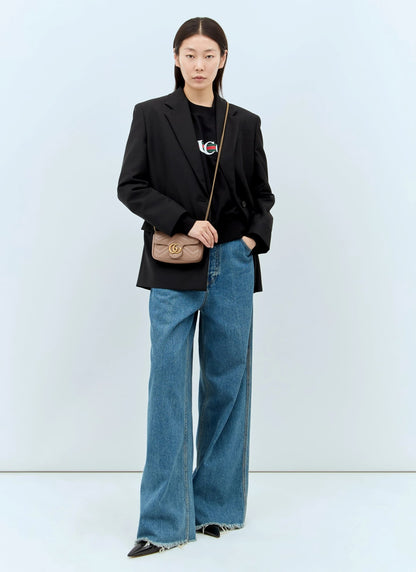 Person wearing a black blazer and blue jeans with a Gucci GG Marmont Matelassé Leather Mini Bag Dusty Pink 476433 DTDCT 5729 on a light blue background