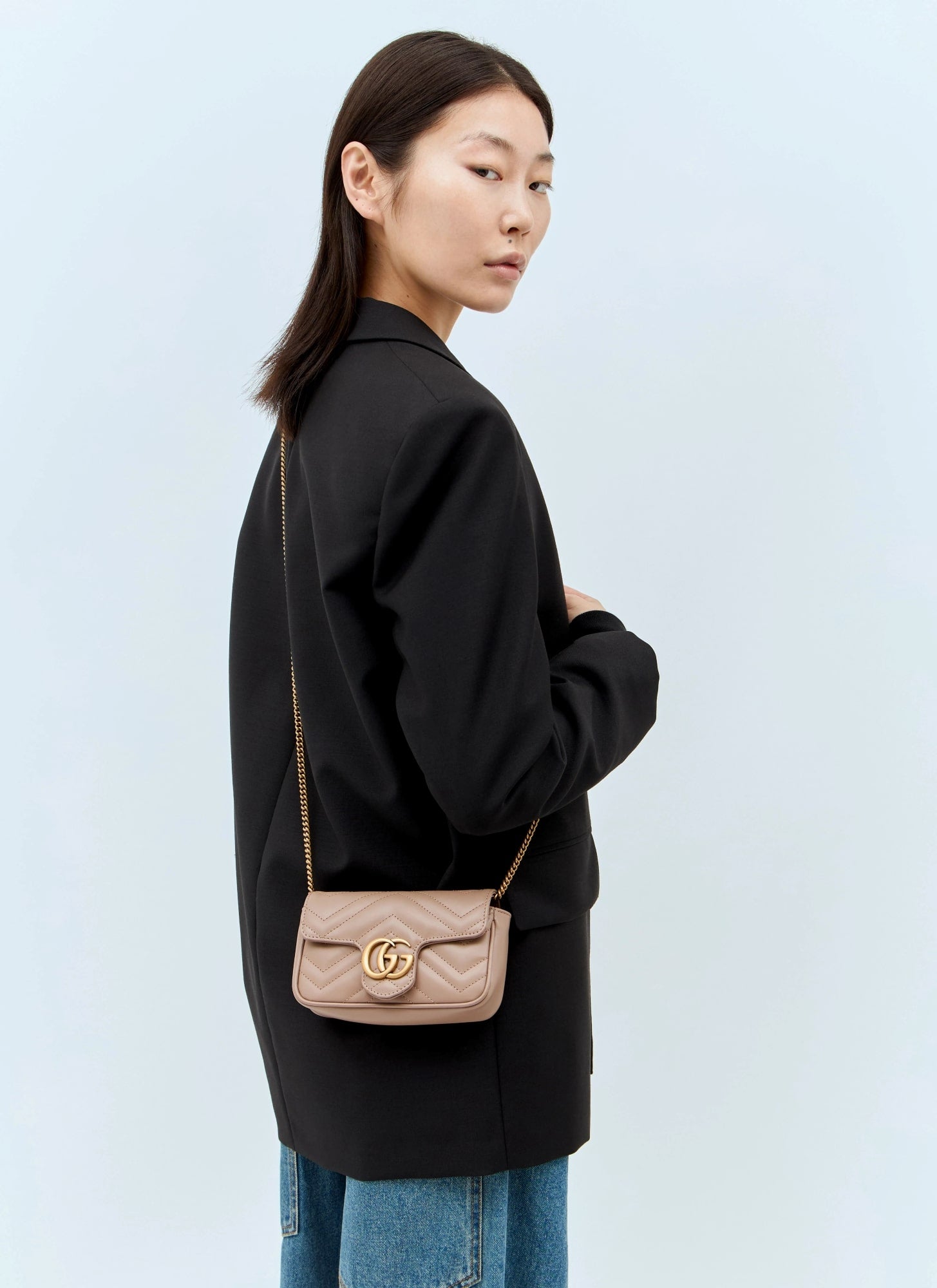 Woman wearing a black coat with a Gucci GG Marmont Matelassé Leather Mini Bag Dusty Pink 476433 DTDCT 5729 on a light blue background