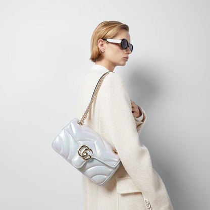 Woman holding a Gucci GG Marmont Medium Shoulder Bag Blue Iridescent 443497 AAC2U 4923 with a gold chain strap against a light gray background