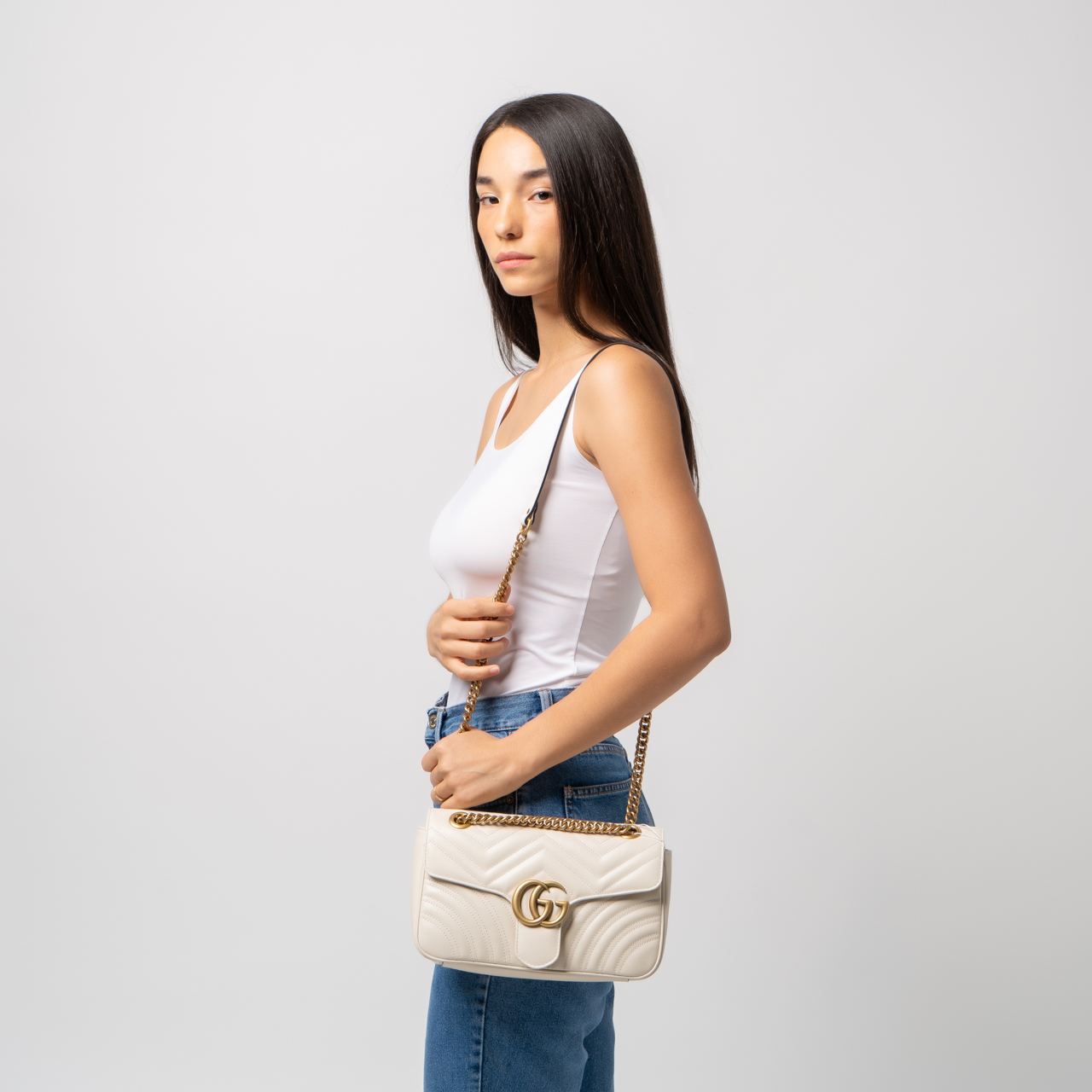 Woman holding a Gucci GG Marmont Medium Shoulder Bag White 443497 dtdit 9022 with a gold chain strap against a light gray background