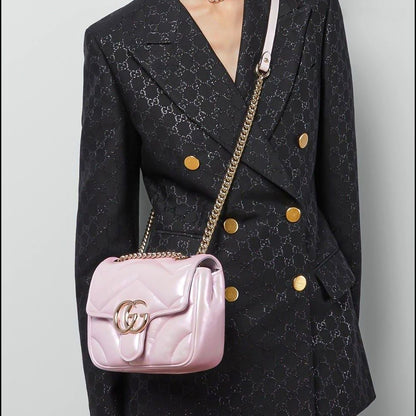 Person wearing a black patterned coat with a Gucci GG Marmont Iridescent Mini Crossbody Bag in Pink 739682 AAC2U 5826 featuring gold accents.