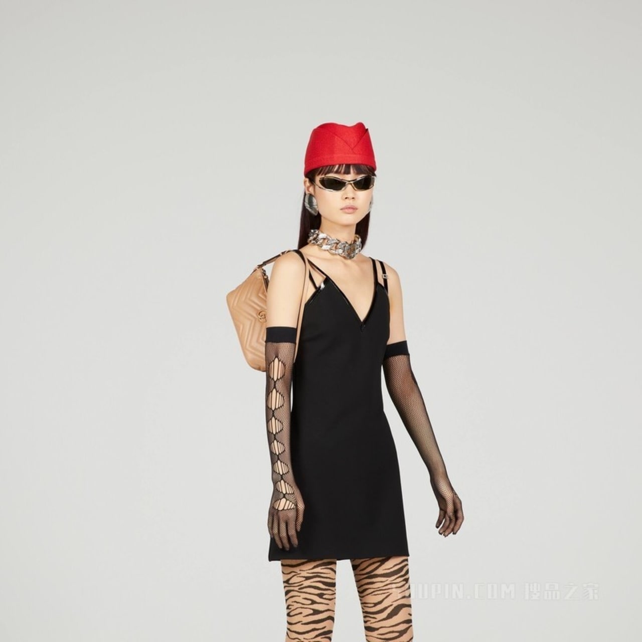 Model wearing a black dress with sheer sleeves, red hat, and zebra print leggings and holding Gucci GG Marmont Shoulder Bag Rose Beige 739166daaah2754 on a gray background