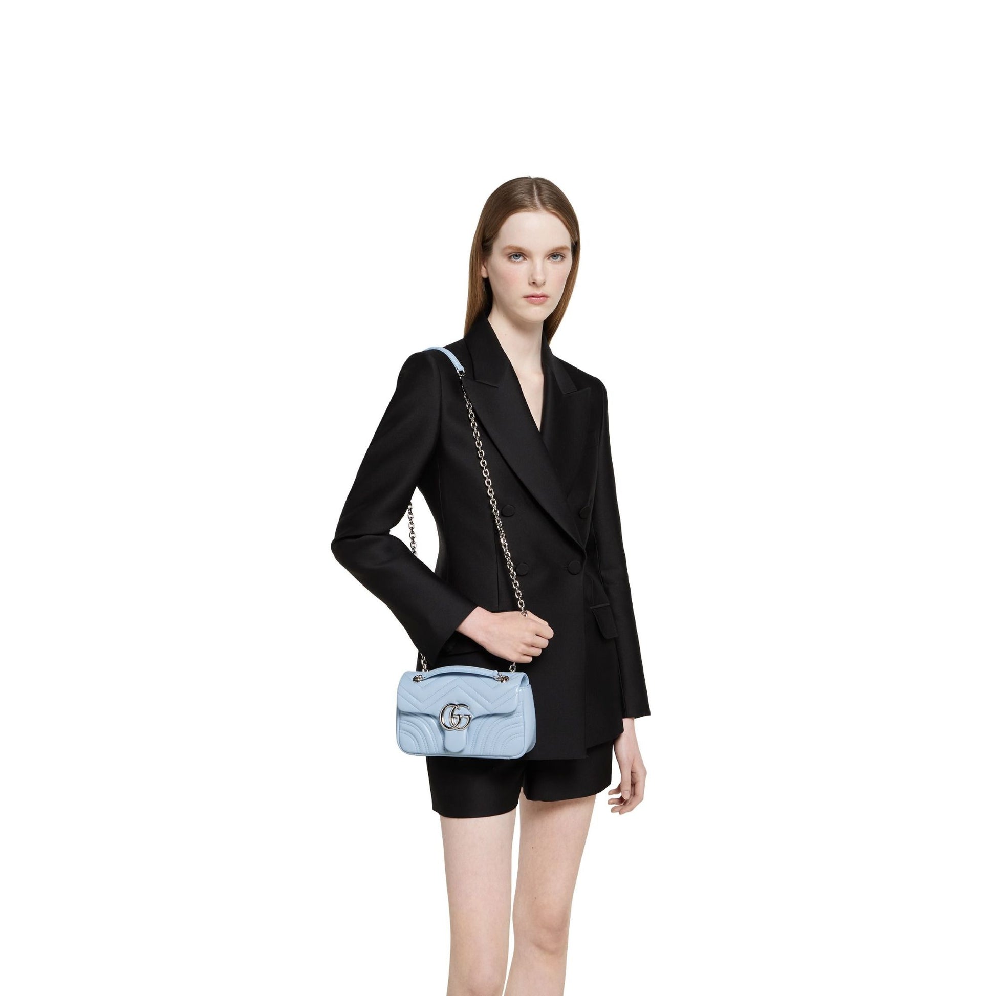 Woman wearing a black blazer and holding a Gucci GG Marmont Small Shoulder Bag Light Blue Leather 837280 AAFA1 4928 on a white background