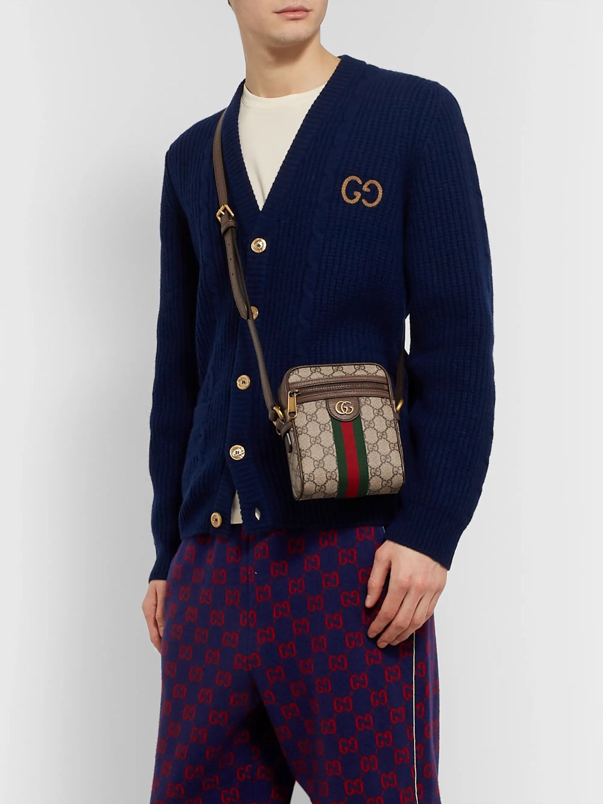 Person wearing a navy cardigan with a Gucci logo, holding a Gucci GG Supreme Ophidia Shoulder Bag 598127 96IWT 8745 against a white background