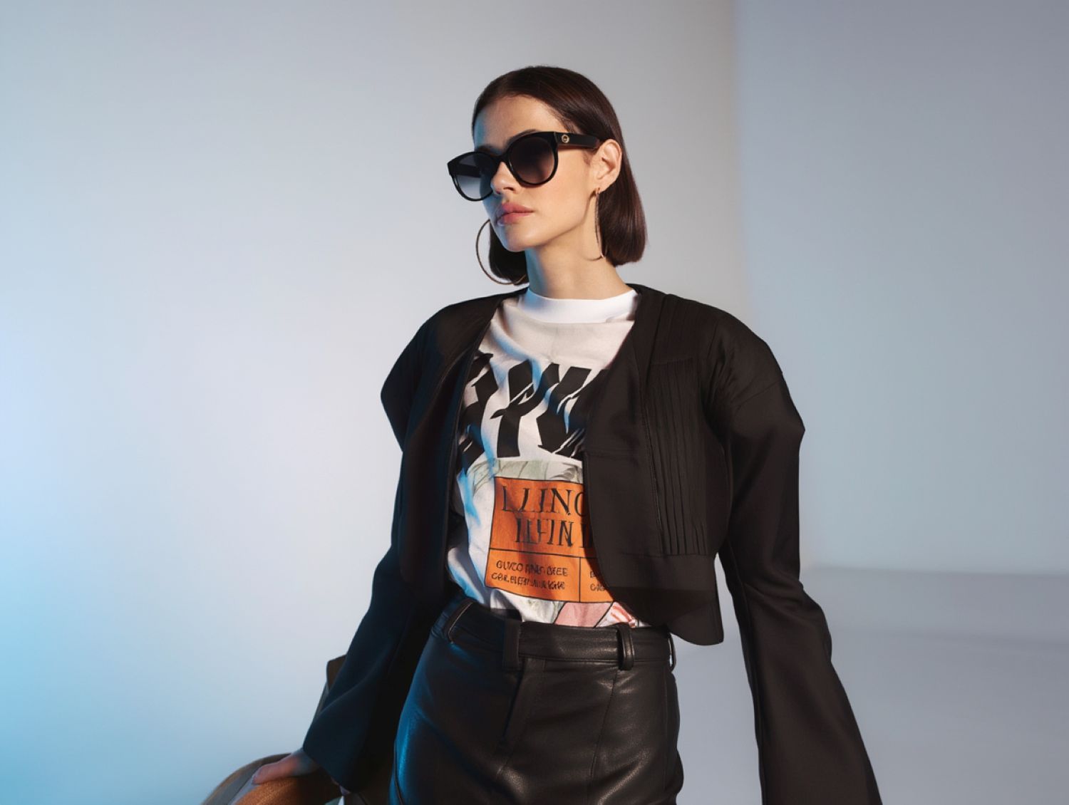 Person wearing a black jacket, graphic t-shirt, and Gucci GG0035SN-001 Round Sunglasses against a light background