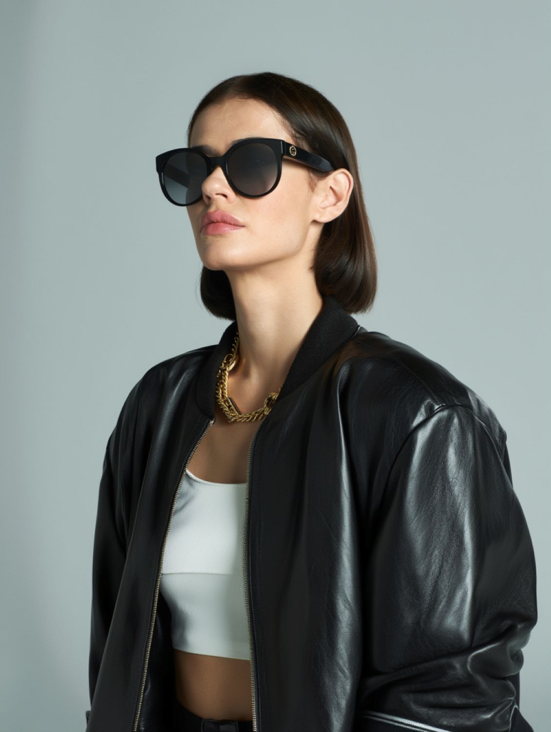 Woman wearing a black leather jacket and Gucci GG0035SN-001 Round Sunglasses against a gray background