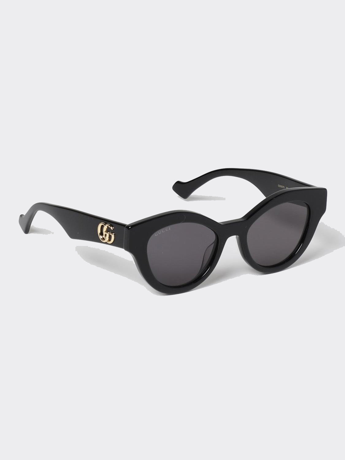 Gucci GG0957S 002 Black Butterfly Rounded Sunglasses with dark gray lenses and a gold interlocking GG logo on the temple, shown on a light gray background.