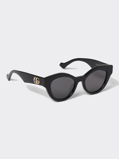 Gucci GG0957S 002 Black Butterfly Rounded Sunglasses with dark gray lenses and a gold interlocking GG logo on the temple, shown on a light gray background.
