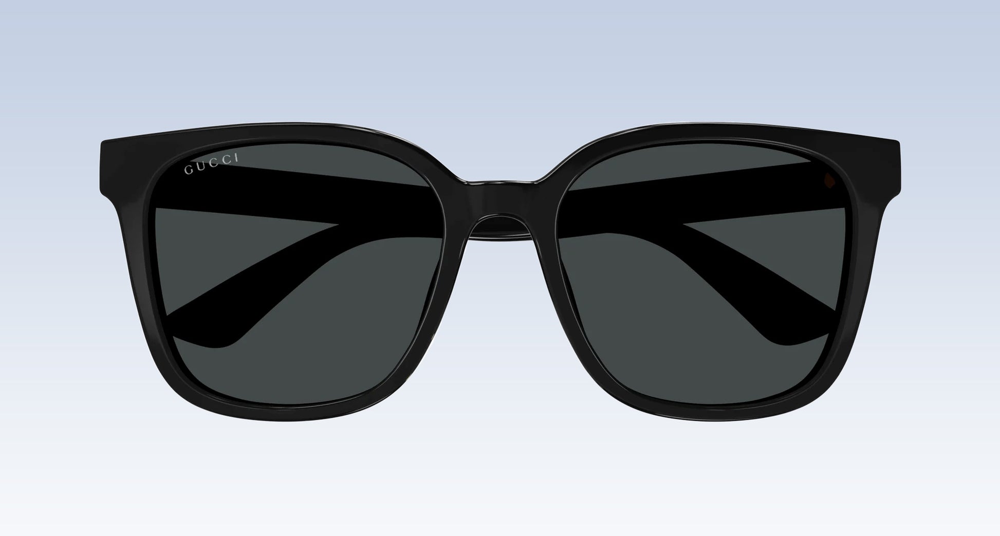 Gucci GG1346SK 001 Black Square Oversize Sunglasses with a glossy black frame and dark gray lenses, shown from the front against a light blue gradient background.
