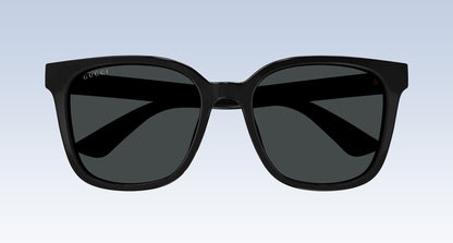 Gucci GG1346SK 001 Black Square Oversize Sunglasses with a glossy black frame and dark gray lenses, shown from the front against a light blue gradient background.