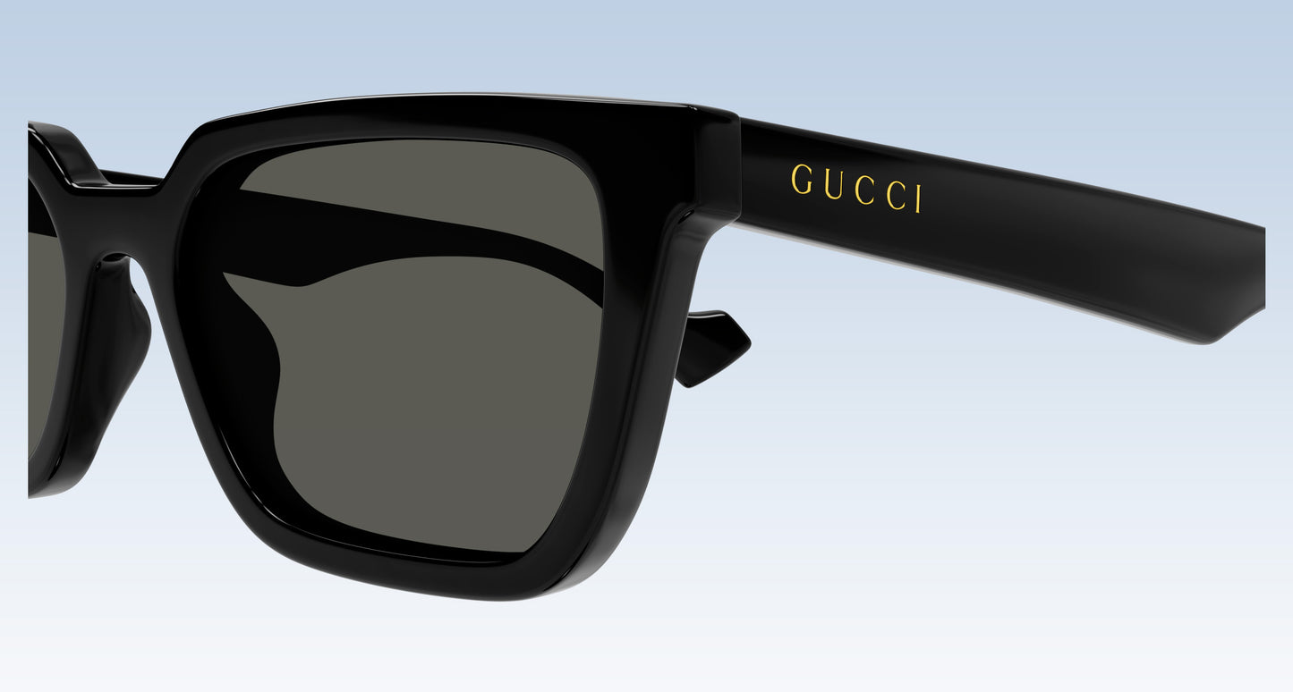 Gucci GG1539S 001 Black Rectangular Sunglasses with a glossy black frame and dark gray lenses, featuring the gold 'GUCCI' logo on the temple arm, set against a light blue gradient background.