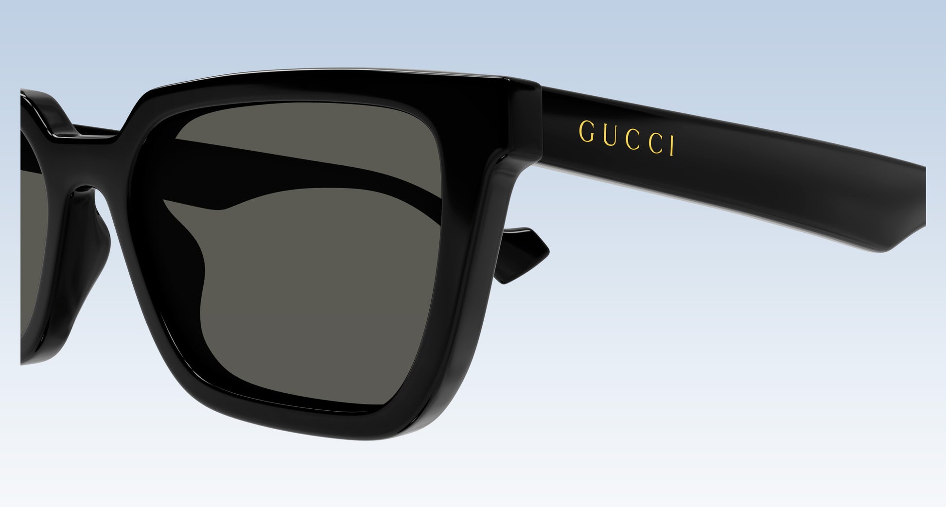 Gucci GG1539S 001 Black Rectangular Sunglasses with a glossy black frame and dark gray lenses, featuring the gold 'GUCCI' logo on the temple arm, set against a light blue gradient background.