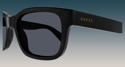 Gucci GG1583S 001 Black Squared Sunglasses with a glossy black frame and dark gray lenses, featuring the gold 'GUCCI' logo on the temple arm, set against a blue-to-gray gradient background.
