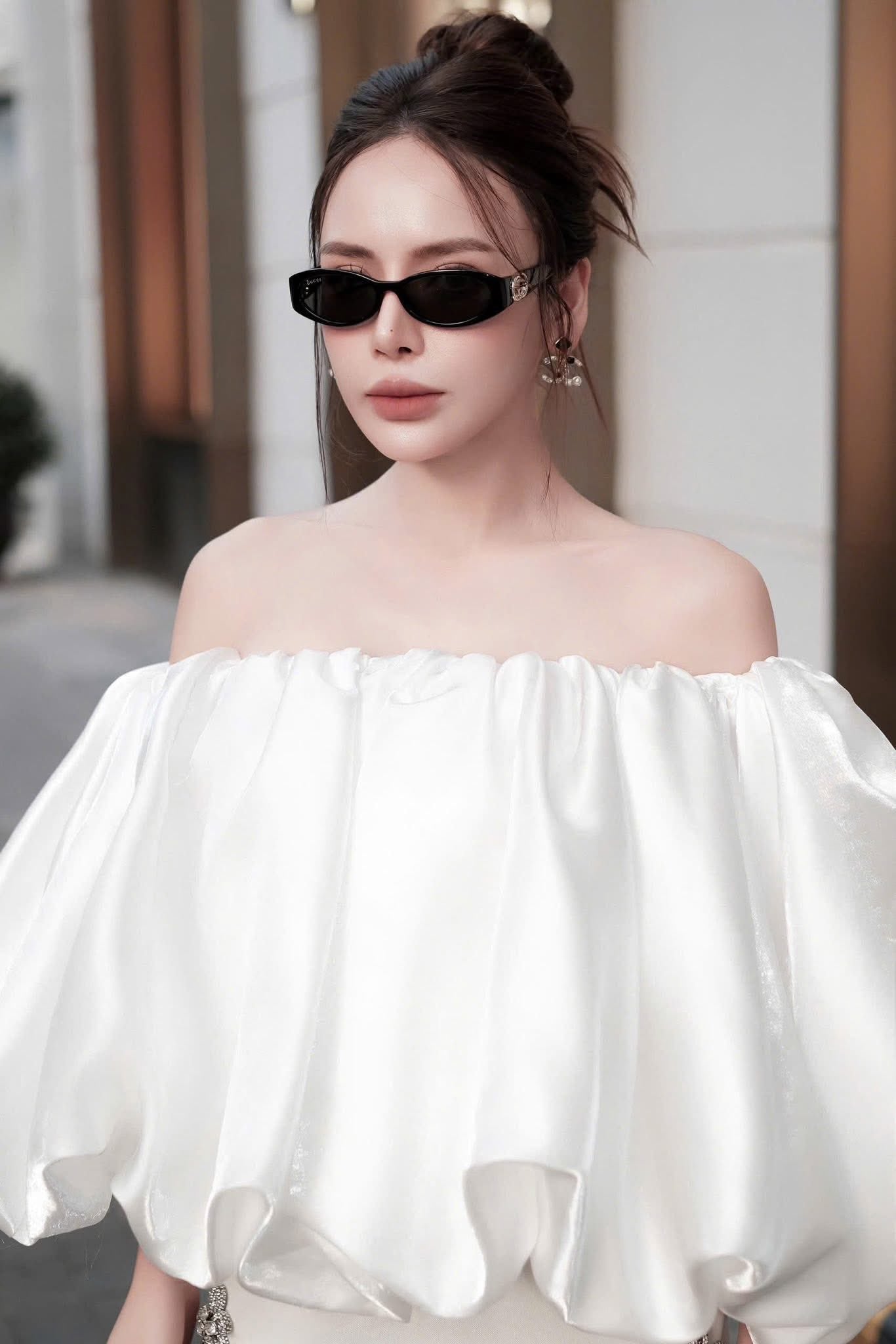 Woman wearing a white off-shoulder top with Gucci GG1660S 001 Oval Frame Sunglasses 785560 J1691 1012 and a blurred background